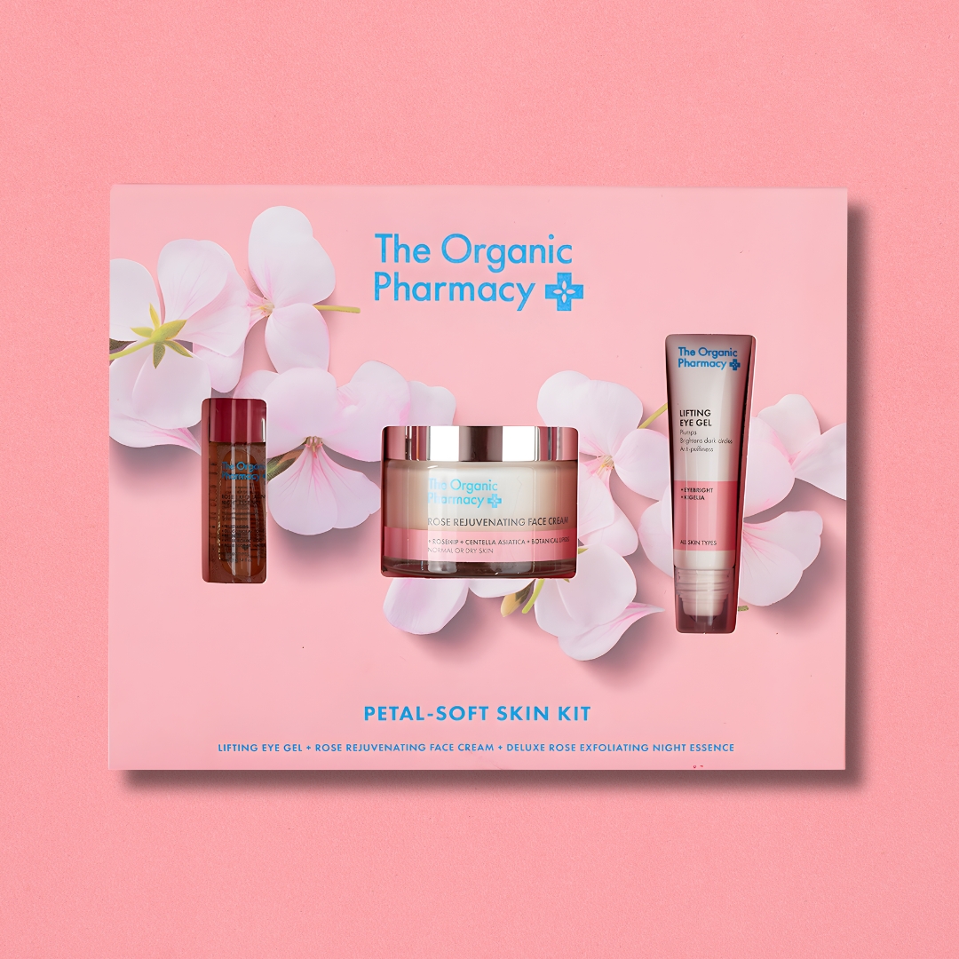 The Organic Pharmacy Petal-Soft Skin Kit featuring lifting eye gel, rose rejuvenating face cream, and deluxe rose exfoliating night essence on pink floral background